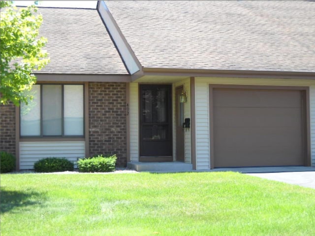 view of front of property featuring driveway, roof with shingles, brick siding, a front lawn, and an attached garage