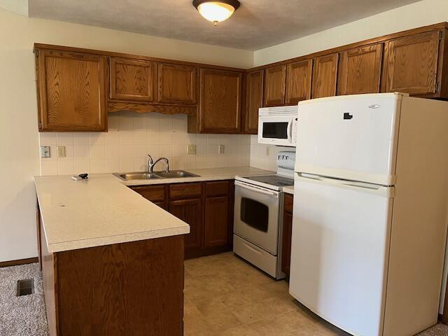 kitchen featuring decorative backsplash, a sink, light countertops, a peninsula, and white appliances