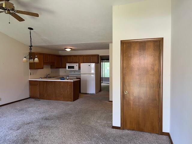 kitchen featuring a peninsula, light carpet, and white appliances