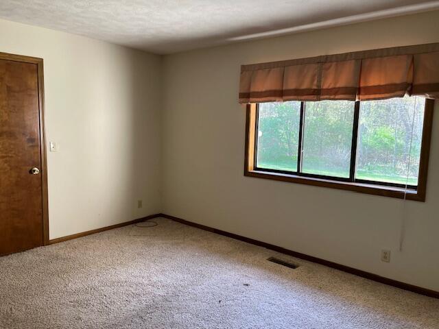 empty room with baseboards, visible vents, a textured ceiling, and light colored carpet