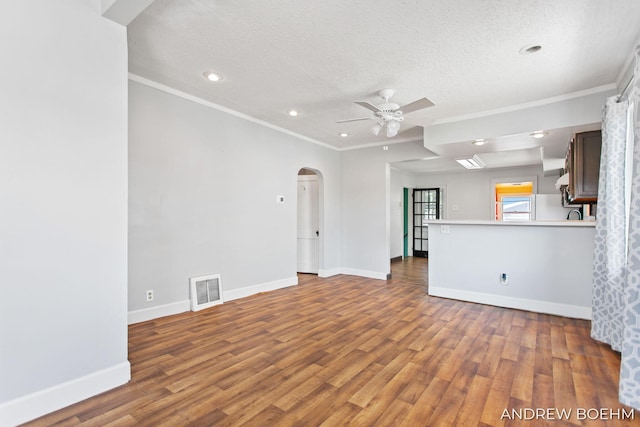 unfurnished living room featuring ceiling fan, visible vents, crown molding, arched walkways, and wood finished floors