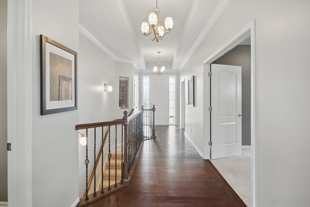 hallway with a notable chandelier, a raised ceiling, hardwood / wood-style floors, baseboards, and an upstairs landing