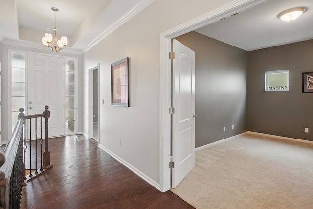 hallway featuring an inviting chandelier, ornamental molding, wood finished floors, baseboards, and a raised ceiling