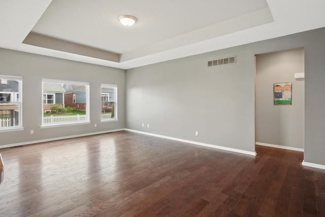 empty room with a raised ceiling, baseboards, dark wood-style flooring, and visible vents