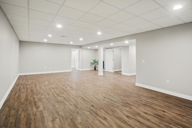 unfurnished living room with a paneled ceiling, recessed lighting, baseboards, and wood finished floors