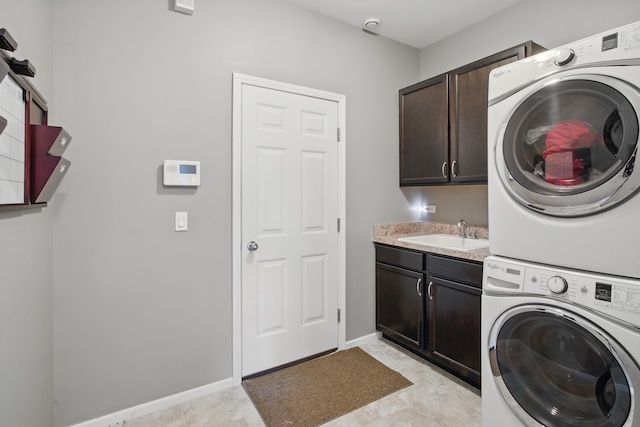 laundry area with cabinet space, stacked washer / drying machine, baseboards, and a sink
