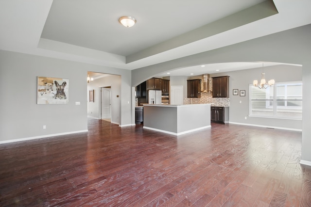 unfurnished living room with dark wood-style flooring, baseboards, a chandelier, a tray ceiling, and arched walkways
