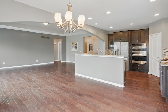 kitchen with dark brown cabinets, arched walkways, open floor plan, tasteful backsplash, and visible vents