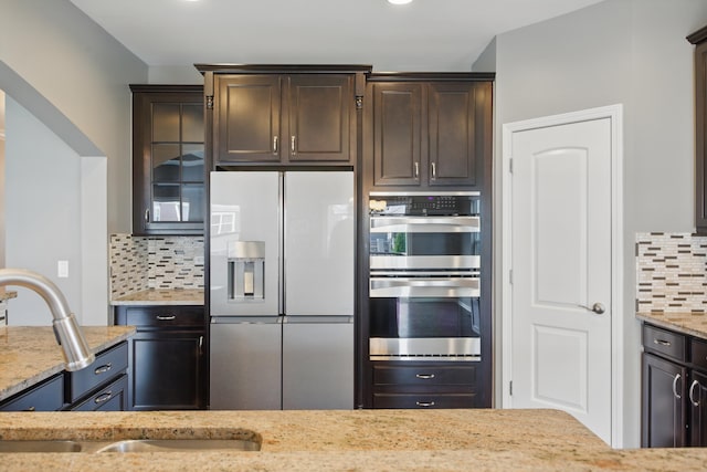 kitchen featuring light stone countertops, a sink, double oven, decorative backsplash, and fridge with ice dispenser