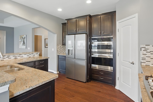 kitchen featuring light stone countertops, a sink, double oven, decorative backsplash, and fridge with ice dispenser