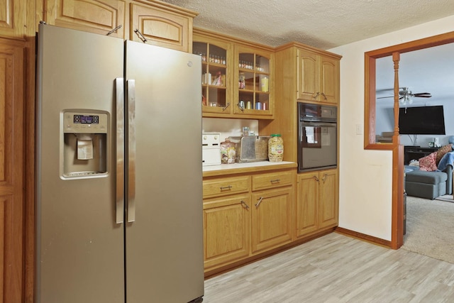 kitchen with oven, light countertops, light wood-style flooring, stainless steel refrigerator with ice dispenser, and glass insert cabinets