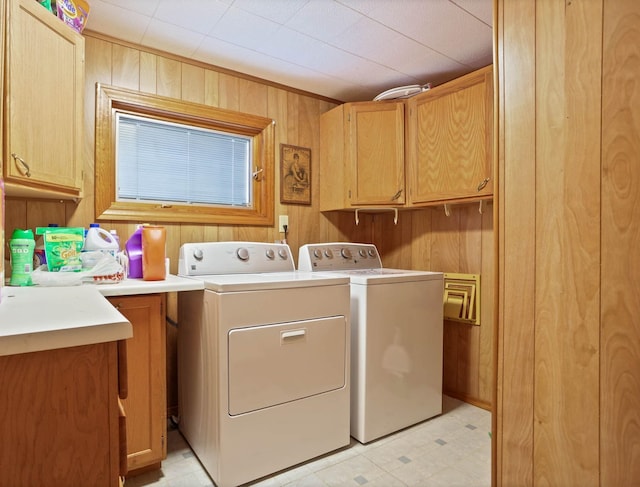 washroom with independent washer and dryer, light floors, wood walls, and cabinet space