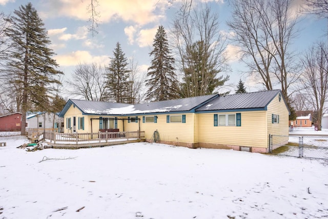 snow covered house with fence, metal roof, and a deck