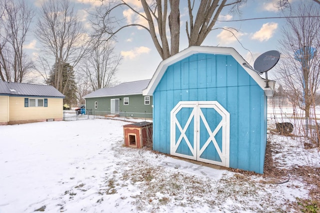 snow covered structure with an outdoor structure, a shed, and fence