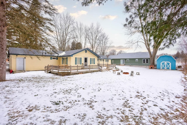 snow covered house featuring a wooden deck, an outdoor structure, and a storage unit