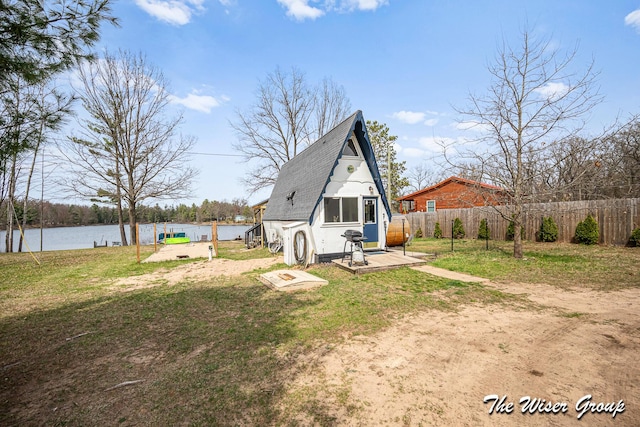 back of house featuring a lawn, a water view, fence, and a shingled roof