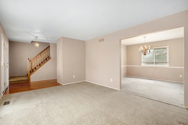 spare room featuring visible vents, carpet flooring, stairway, and an inviting chandelier
