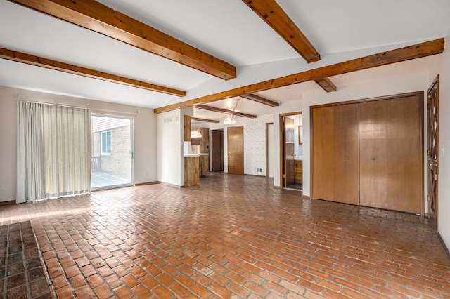 unfurnished living room with baseboards, beam ceiling, and brick floor