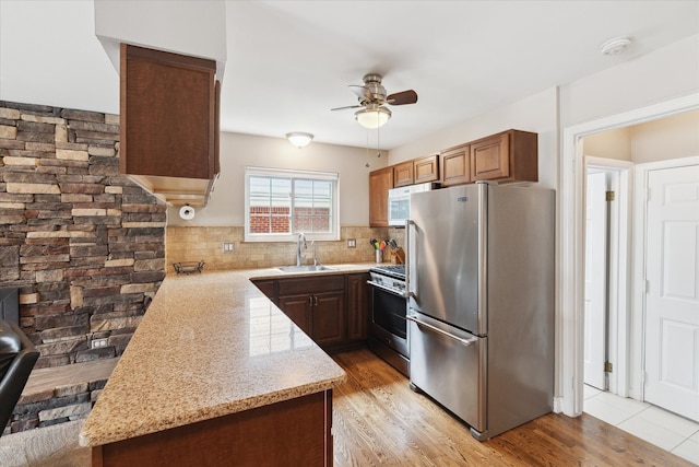 kitchen featuring ceiling fan, appliances with stainless steel finishes, light stone counters, a sink, and backsplash