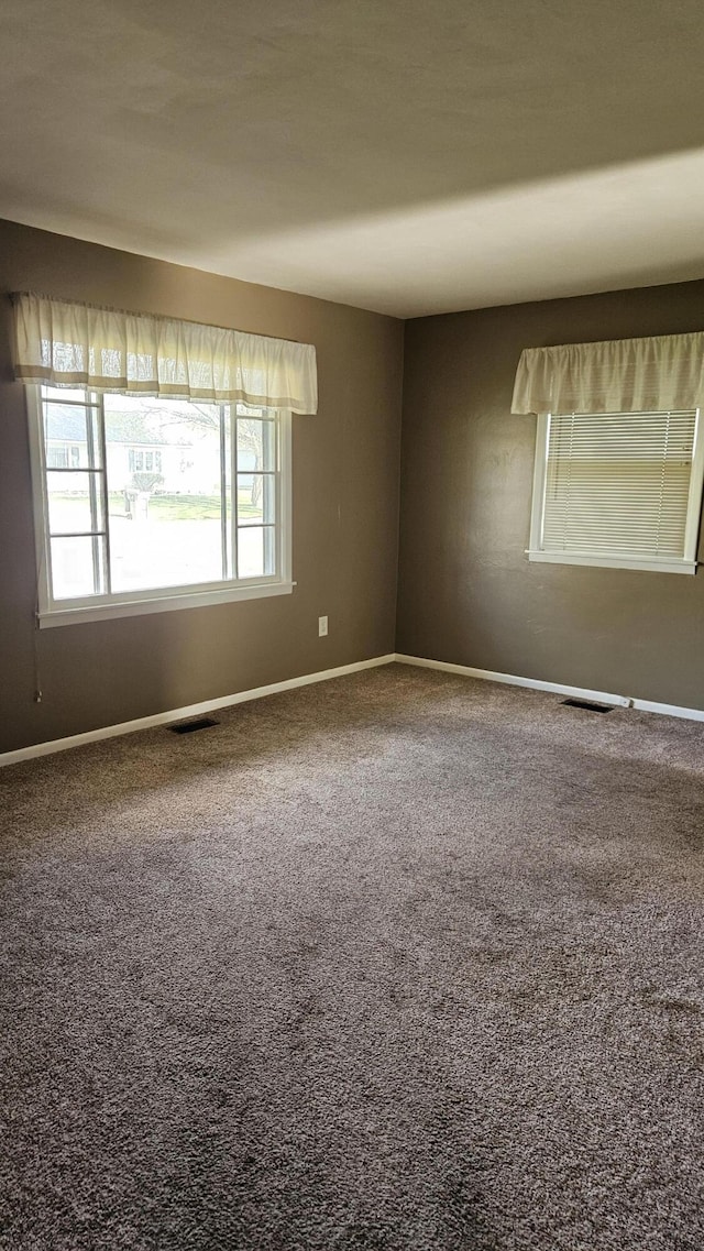 carpeted empty room featuring baseboards and visible vents