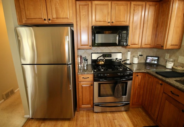 kitchen with brown cabinetry, backsplash, visible vents, dark stone countertops, and stainless steel appliances
