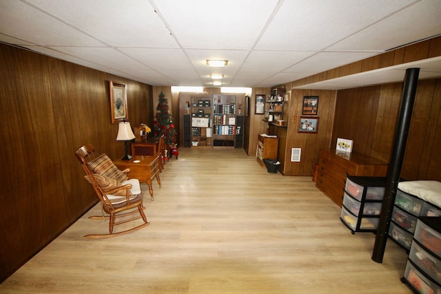 living area with wooden walls, wood finished floors, and a paneled ceiling
