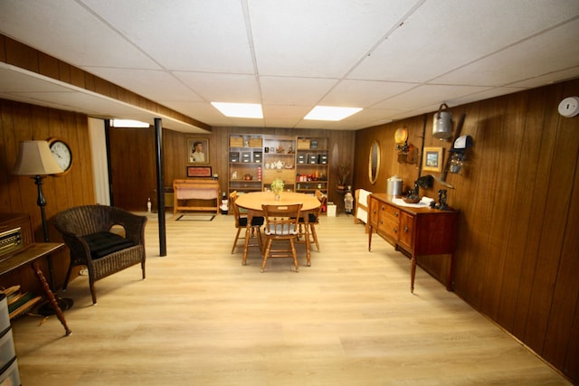 dining space with wood walls, a drop ceiling, and light wood-style floors