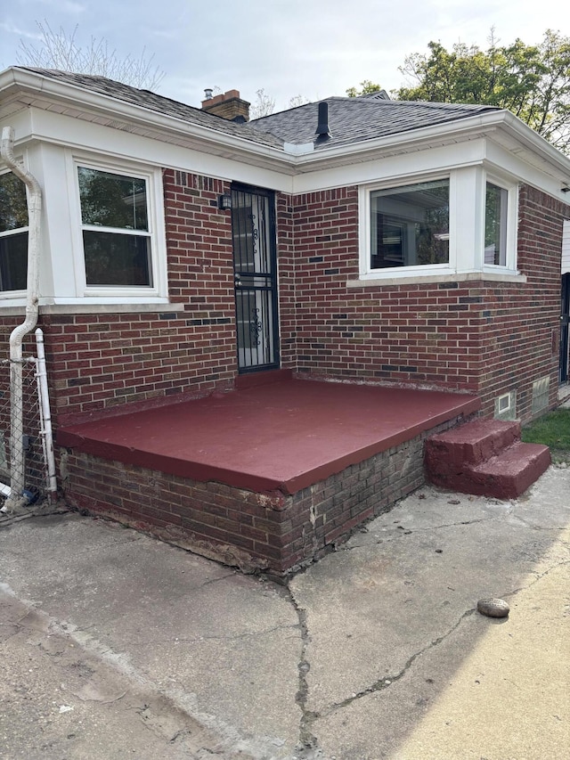 exterior space with brick siding, a shingled roof, and a chimney