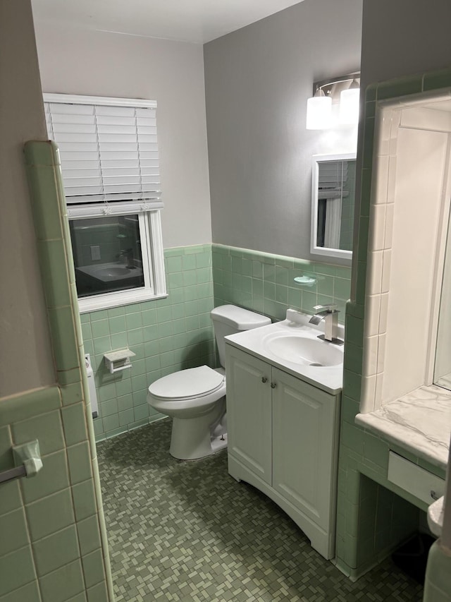 bathroom featuring vanity, a wainscoted wall, toilet, and tile walls