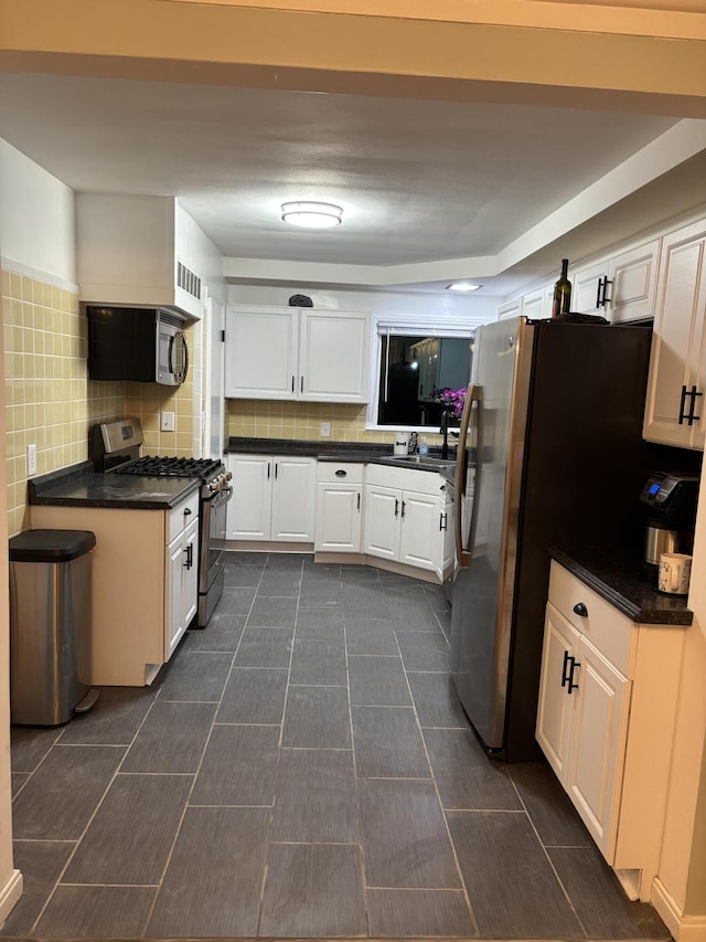 kitchen with dark countertops, appliances with stainless steel finishes, decorative backsplash, and white cabinetry