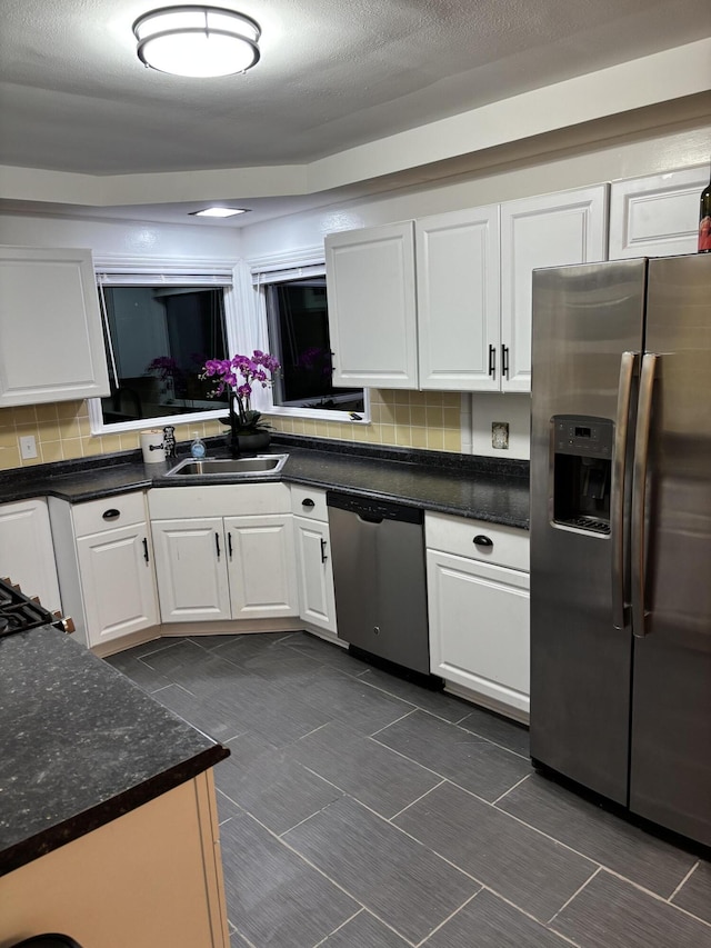 kitchen with white cabinets, a sink, stainless steel appliances, tasteful backsplash, and dark tile patterned flooring