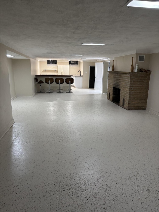 basement with visible vents, baseboards, a brick fireplace, and indoor bar