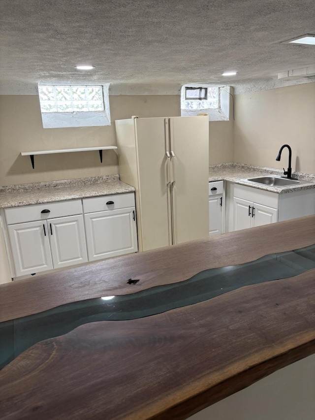 kitchen with a sink, light countertops, a textured ceiling, freestanding refrigerator, and white cabinetry