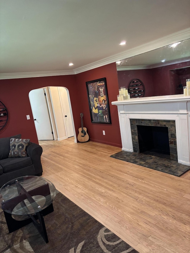 living area with a tiled fireplace, arched walkways, wood finished floors, ornamental molding, and recessed lighting