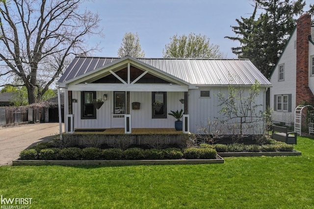 modern inspired farmhouse with a front lawn, a vegetable garden, covered porch, driveway, and metal roof
