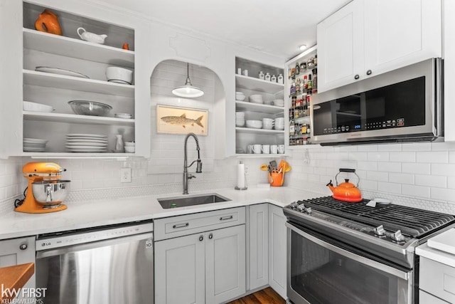 kitchen featuring open shelves, a sink, light countertops, stainless steel appliances, and tasteful backsplash