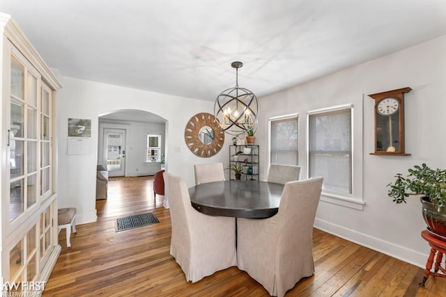 dining area with arched walkways, baseboards, a notable chandelier, and hardwood / wood-style flooring