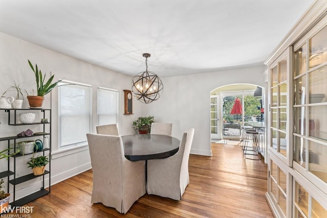 dining area with baseboards, arched walkways, wood finished floors, and a chandelier