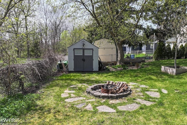 view of yard featuring a storage shed, fence, an outdoor structure, and an outdoor fire pit