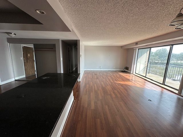 unfurnished living room with recessed lighting, a textured ceiling, dark wood-style floors, and baseboards