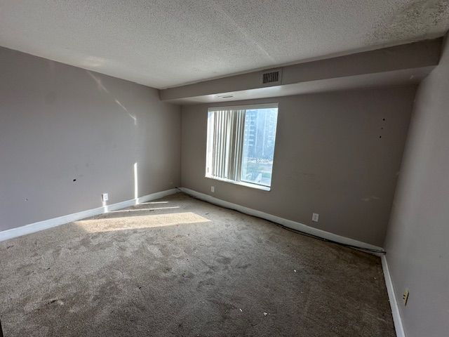 carpeted spare room featuring visible vents, a textured ceiling, and baseboards