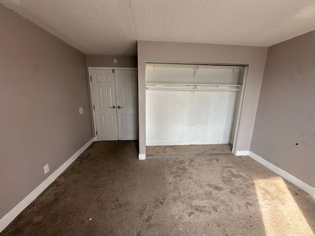 unfurnished bedroom with carpet floors, a textured ceiling, and baseboards