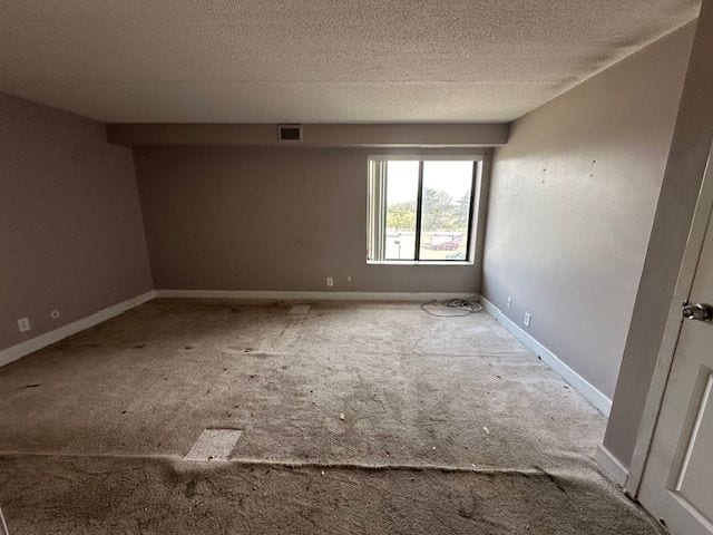 carpeted spare room featuring visible vents, a textured ceiling, and baseboards