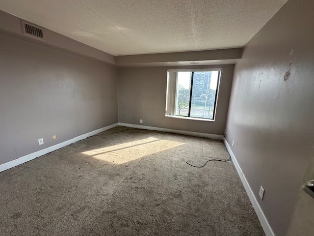 empty room featuring baseboards, carpet, a textured ceiling, and visible vents