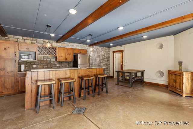 kitchen featuring concrete flooring, appliances with stainless steel finishes, beam ceiling, light countertops, and a kitchen breakfast bar