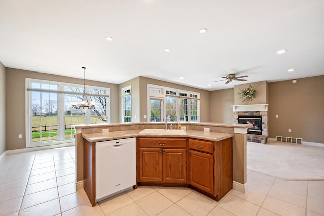 kitchen with visible vents, a stone fireplace, a sink, ceiling fan with notable chandelier, and dishwasher