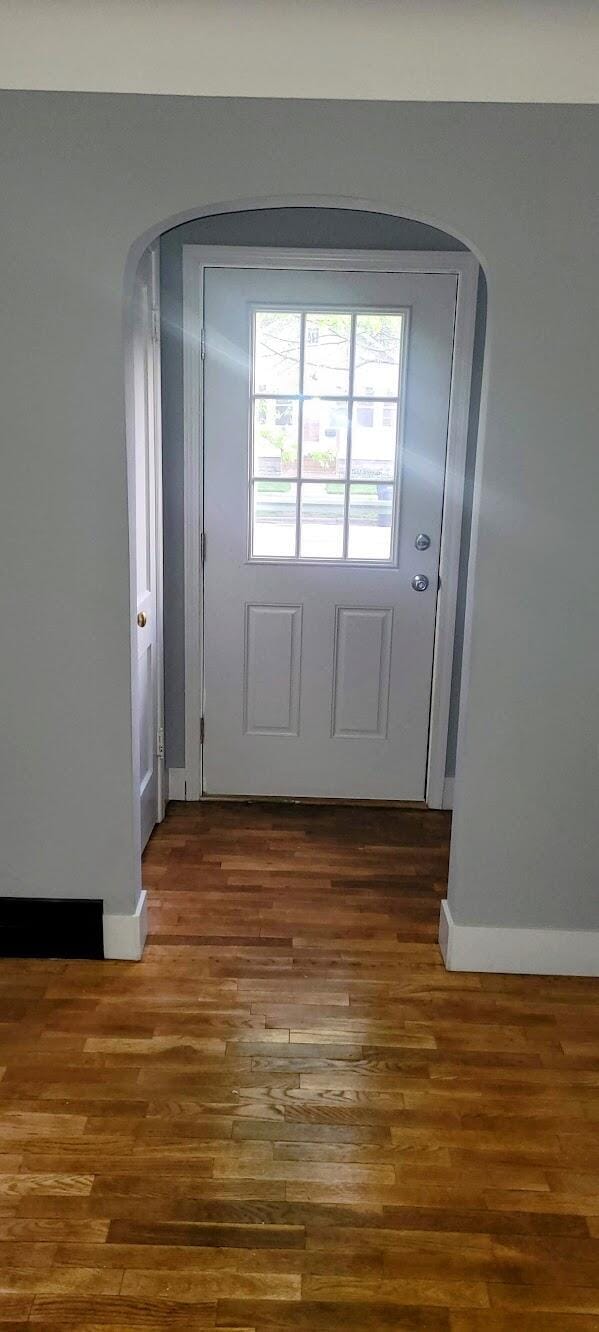 doorway to outside with baseboards, arched walkways, and wood finished floors