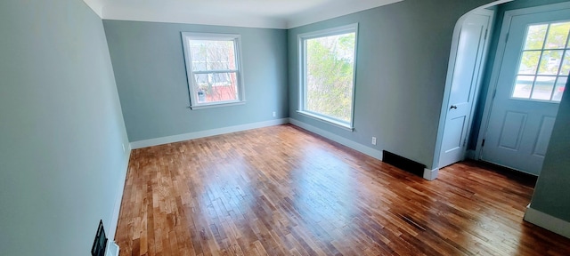 interior space featuring arched walkways, baseboards, a healthy amount of sunlight, and hardwood / wood-style floors