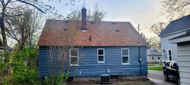 back of property featuring a shingled roof, a chimney, and central AC