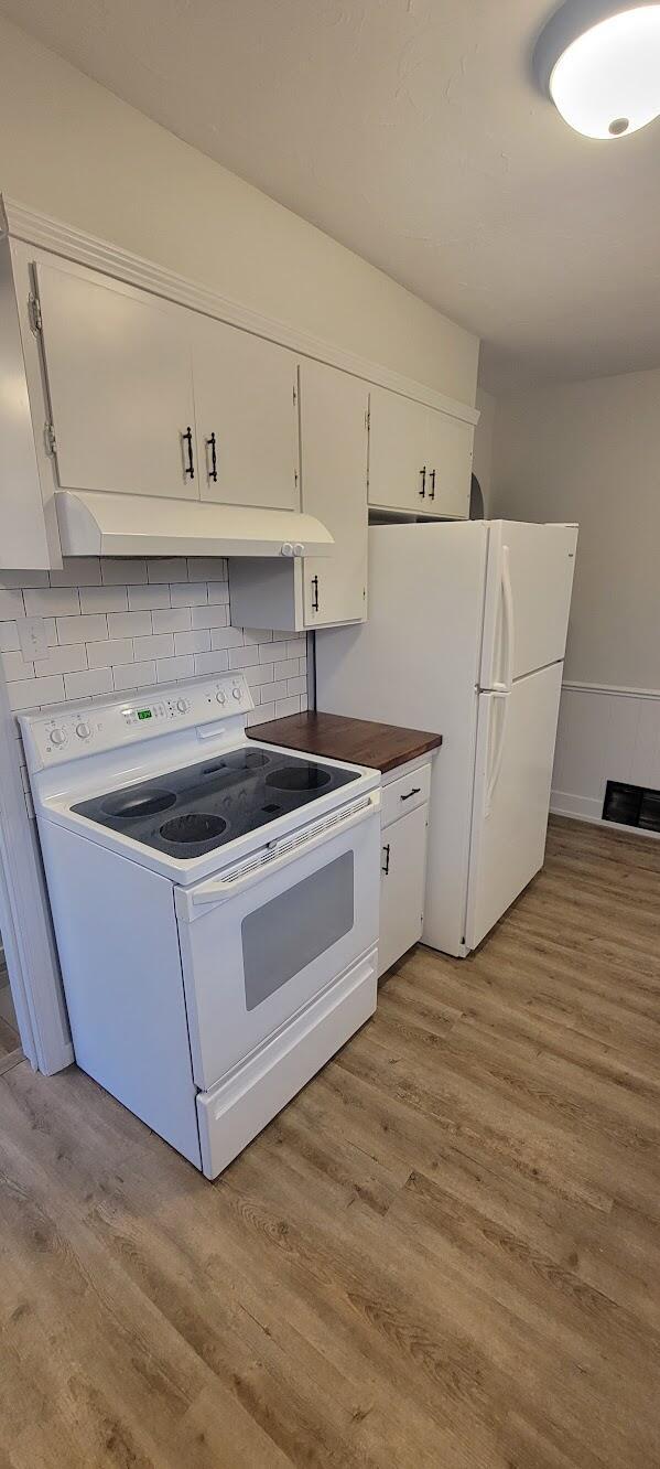 kitchen with light wood finished floors, under cabinet range hood, white appliances, and white cabinetry